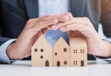 A close-up view of a business person hovering their hands over three wooden blocks that are shaped like houses.