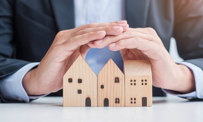 A close-up view of a business person hovering their hands over three wooden blocks that are shaped like houses.