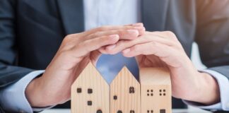 A close-up view of a business person hovering their hands over three wooden blocks that are shaped like houses.