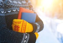 A person in a clack and white sweater and yellow and red knit mittens holds two books outside.