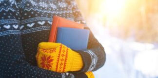 A person in a clack and white sweater and yellow and red knit mittens holds two books outside.